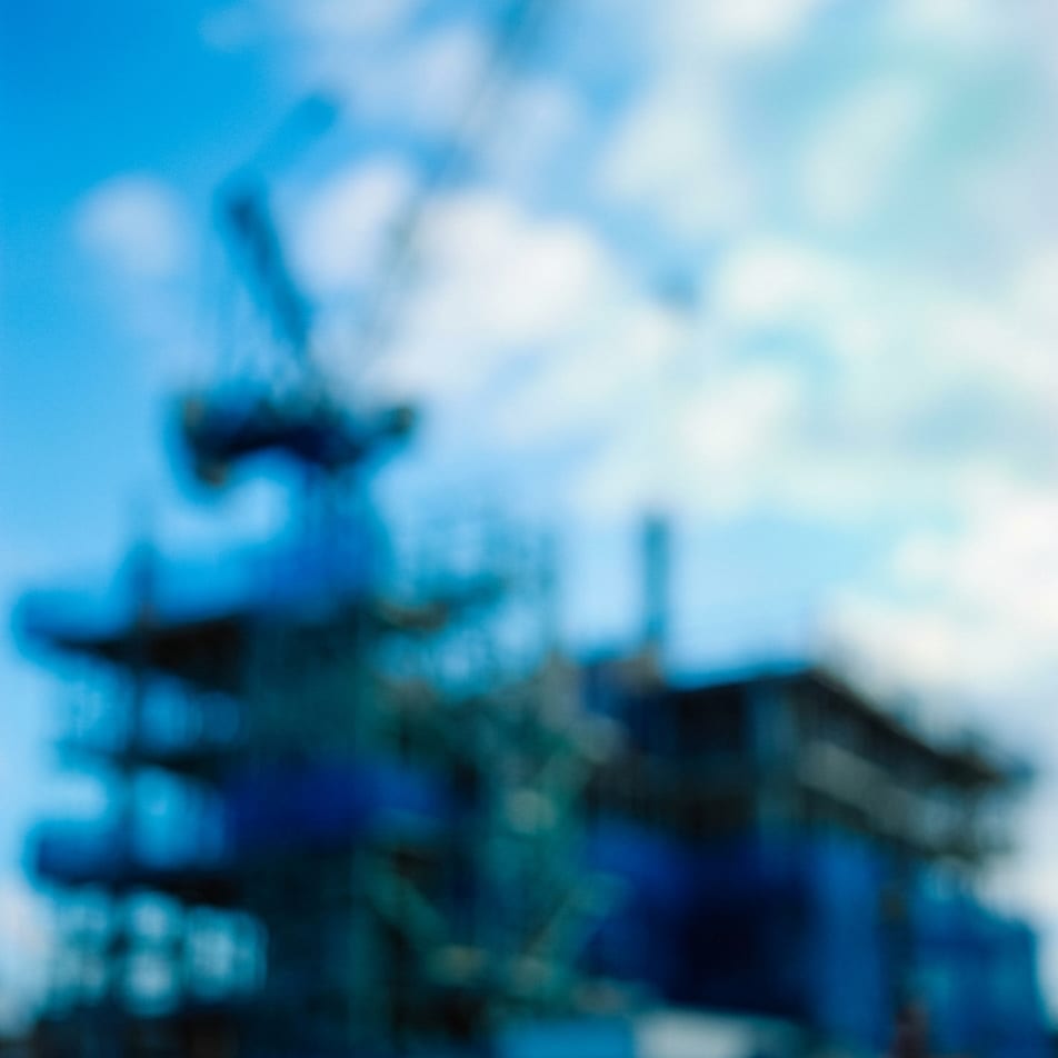 A blurred blue photograph of a building site with a crane against a cloudy sky